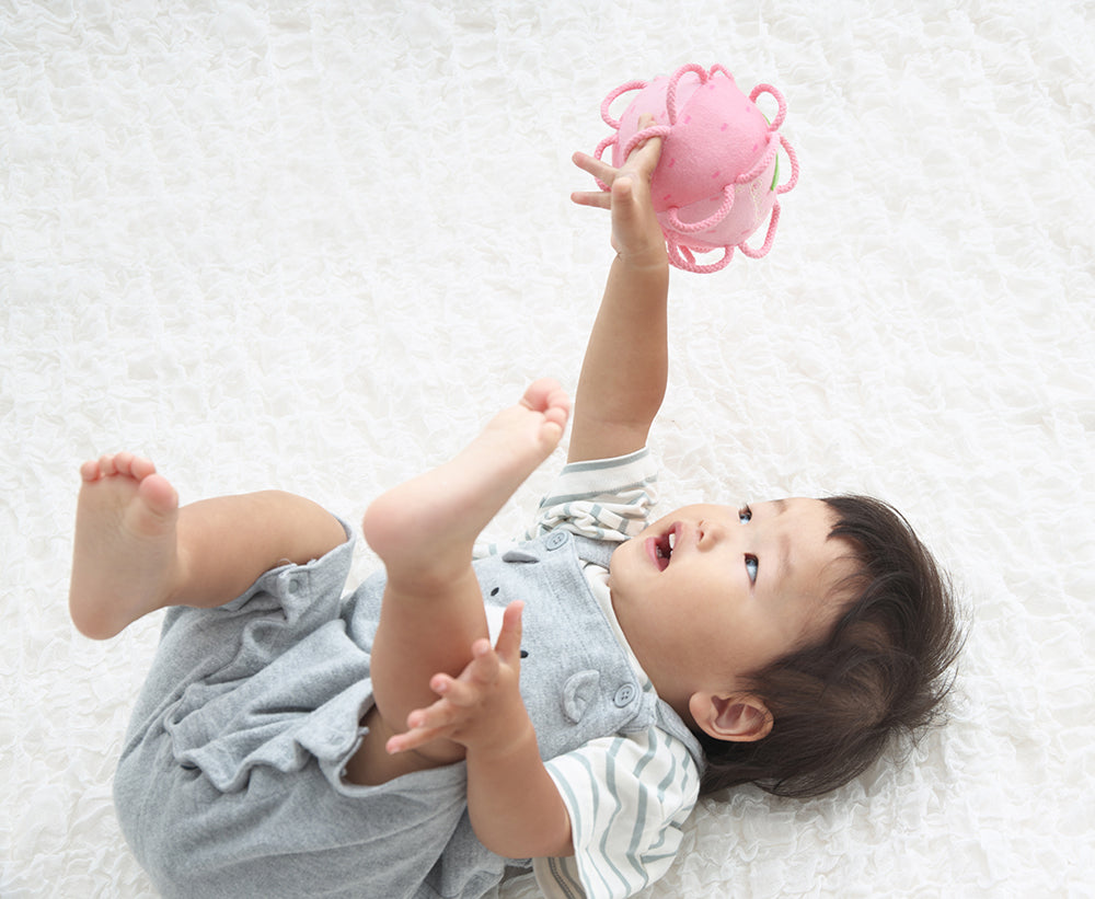 右手にわっかボールももを持って遊ぶ赤ちゃん